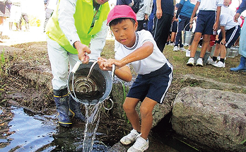 地域の人に手伝ってもらいながら児童が放流する様子