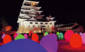 築城400年記念で開催された「チームラボ 福山城 光の祭」の福山城の様子。カラフルな光や色特有の音色が楽しめる卵形体の「自立しつつも呼応する生命」が城のふもとにたくさん置かれている