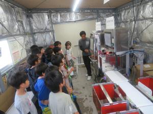 カキの中身をX線で透視し、AIで選別する機械の説明を受けている写真です